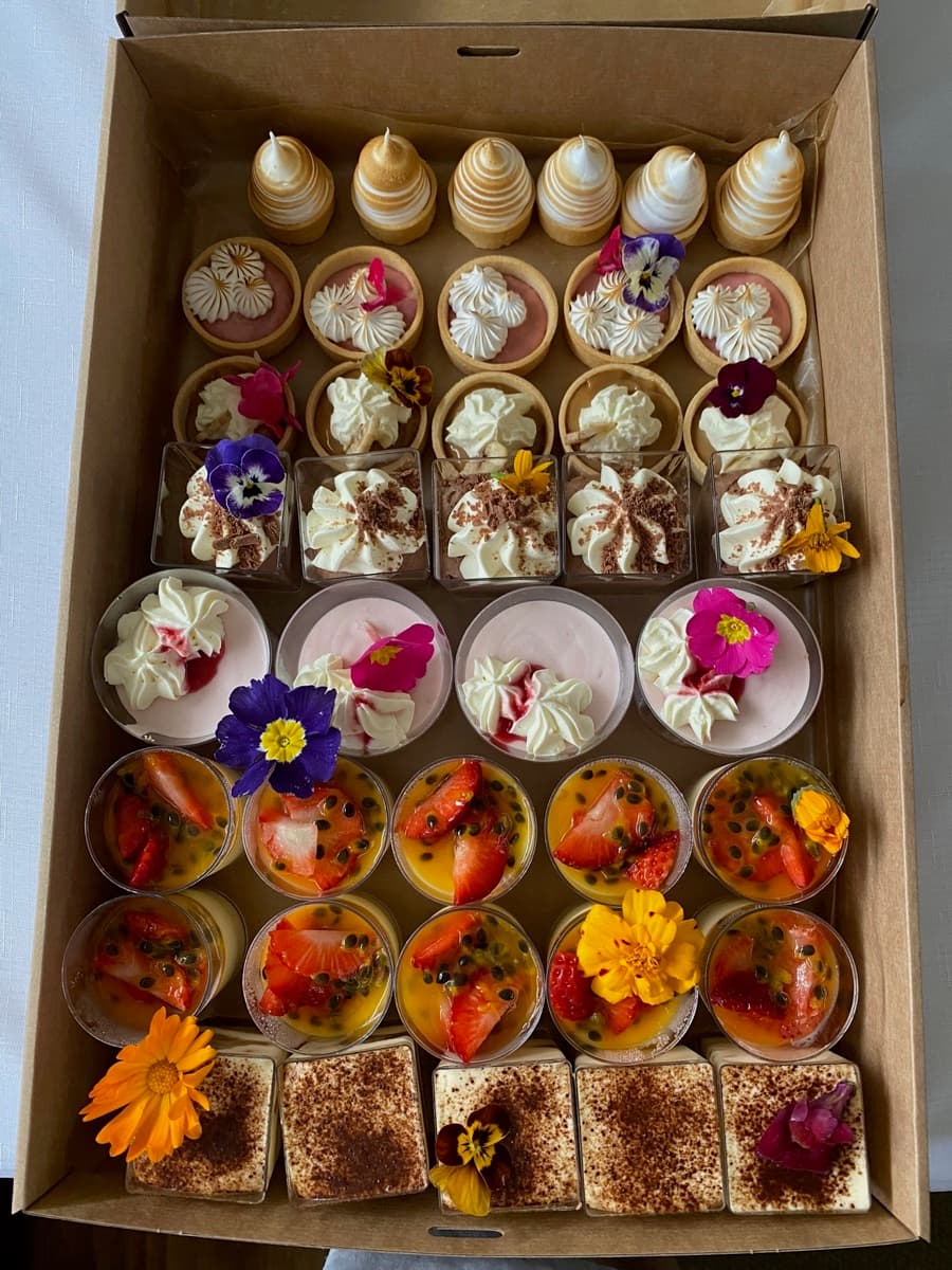 Overhead view of a branded dessert box with meringues, tiramisu, panna cotta fruit cups, cupcakes, and fruit tarts for Adelaide corporate dessert catering