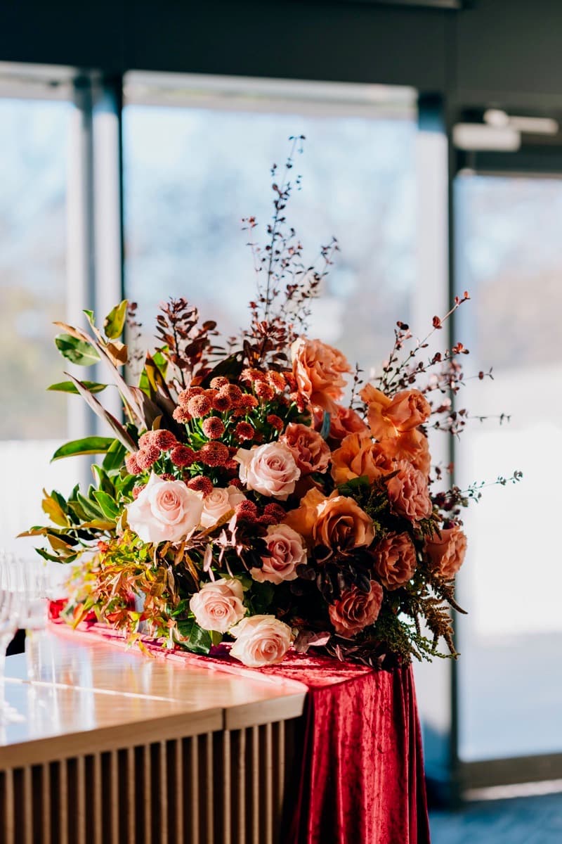 Peach and coral rose arrangement on a velvet runner with warm natural light, Adelaide wedding florals by Event Gourmet