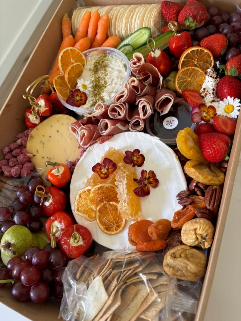 Adelaide cheese platter box with brie, prosciutto, dried oranges, and edible flowers by Event Gourmet